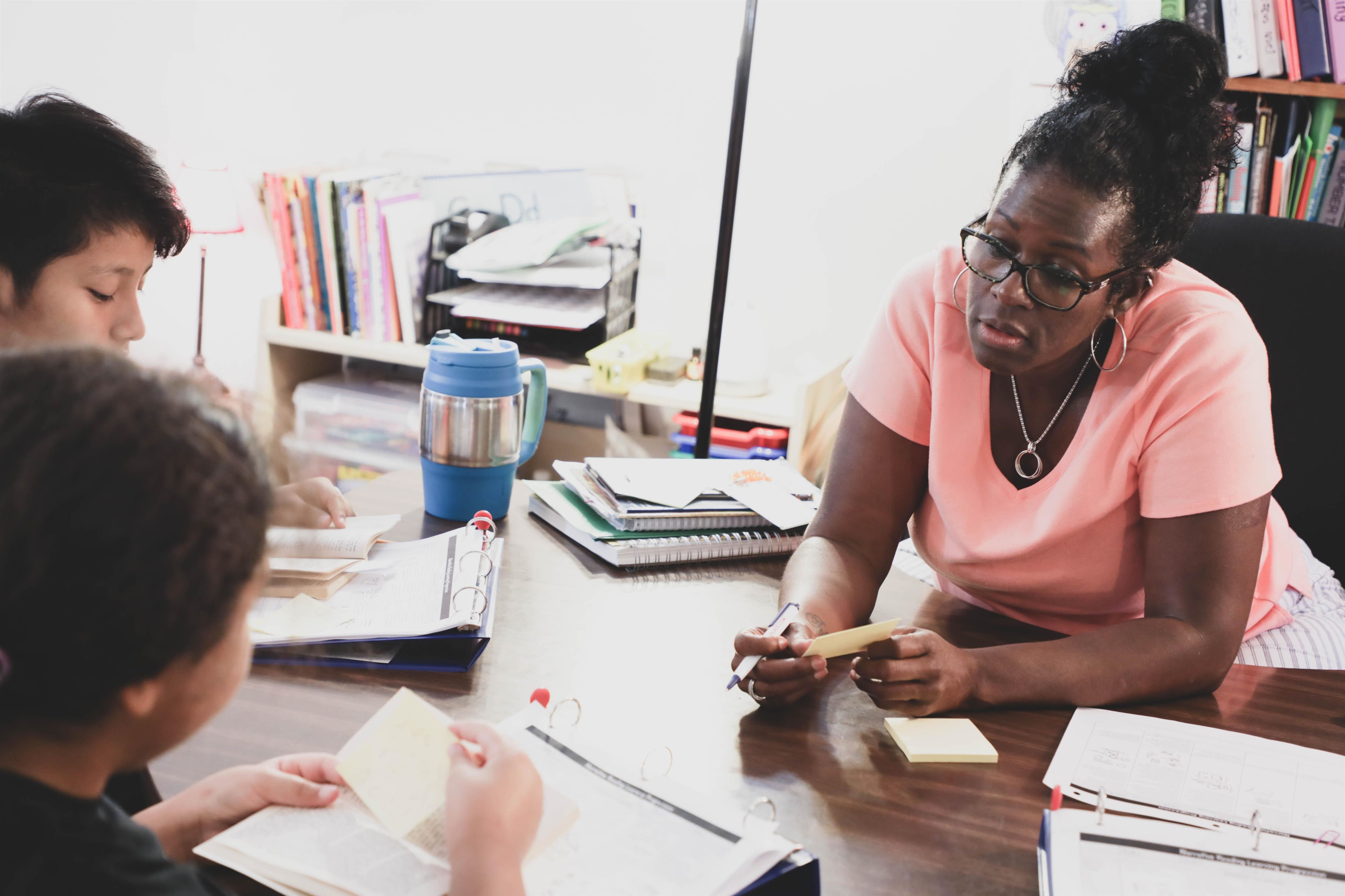 Two students with notecards and open binders conferring with a teacher across a table Two students with notecards and open binders conferring with a teacher across a table